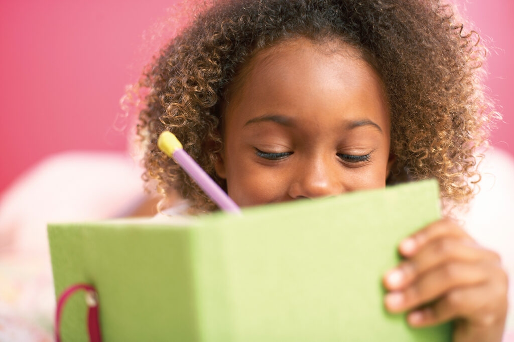 A photo to a young girl writing in her green diary on a pink background