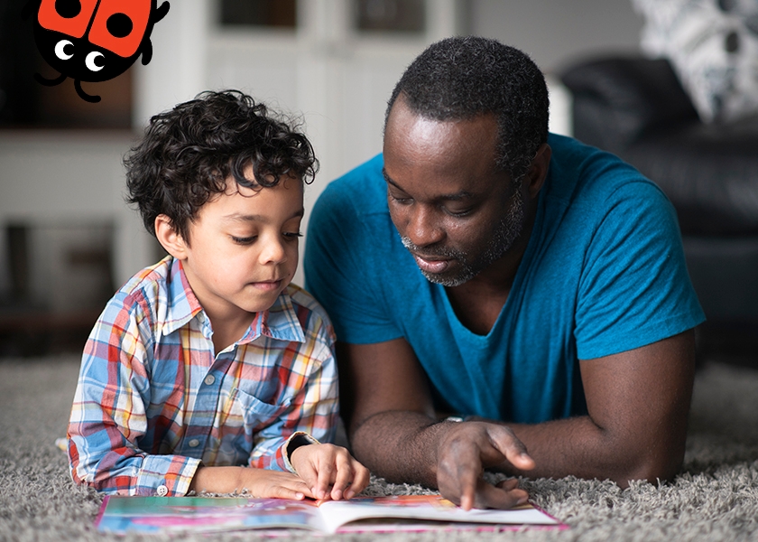 A photo of a father and son laying on the floor whilst reading a book together