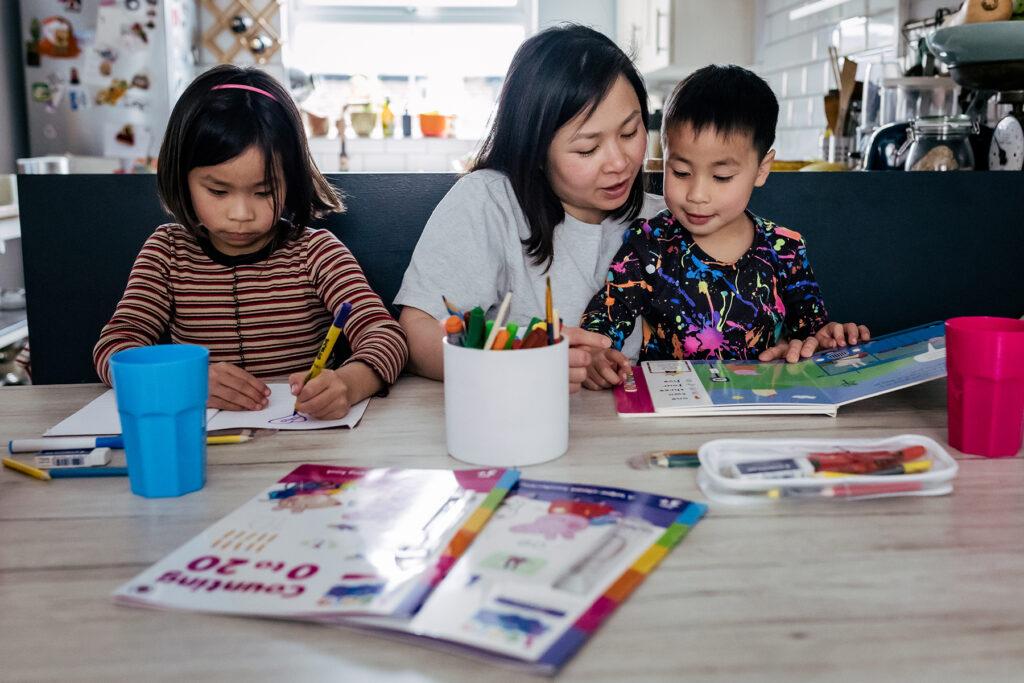 An image of a mother sitting at a table teaching her children.