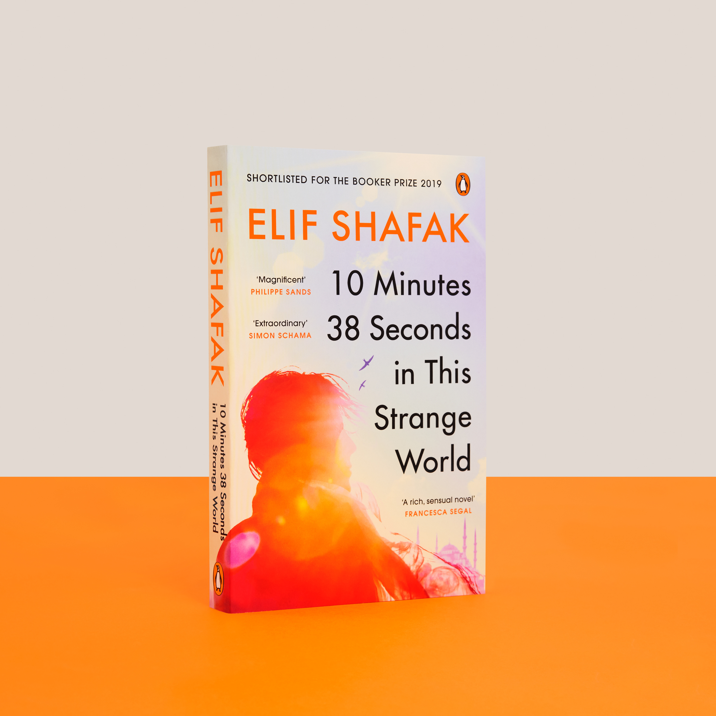 Elif Shafak's 10 Minutes 38 Seconds in This Strange World on an orange and cream background. Photo taken by Stuart Simpson/Penguin.