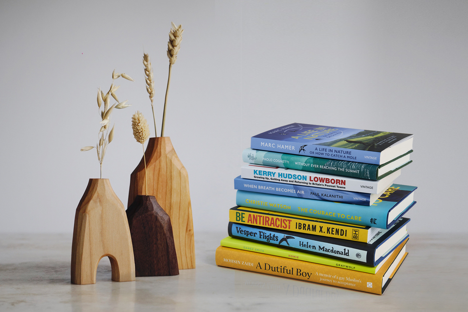 Lifestyle shot of Grain & Knot wooden vase trio next to a stack of blue and yellow Vintage books, against a grey marble background.