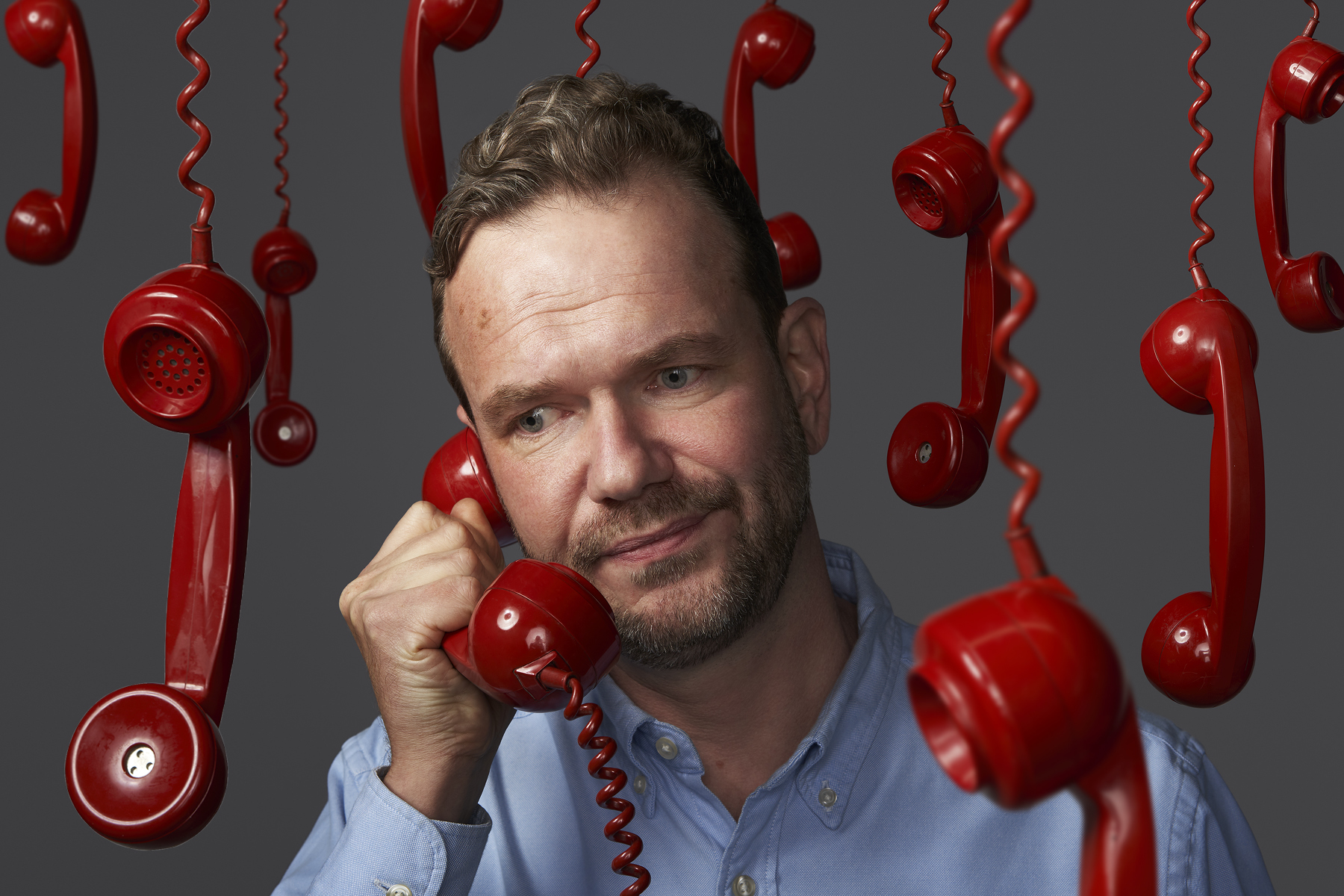 James O'Brien holds a red phone, with other red phones hanging around him.