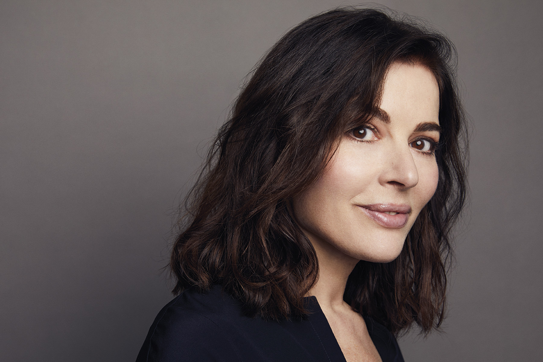 Head and shoulders photo of Nigella Lawson, wearing a black top, turned to the side but looking at the camera.