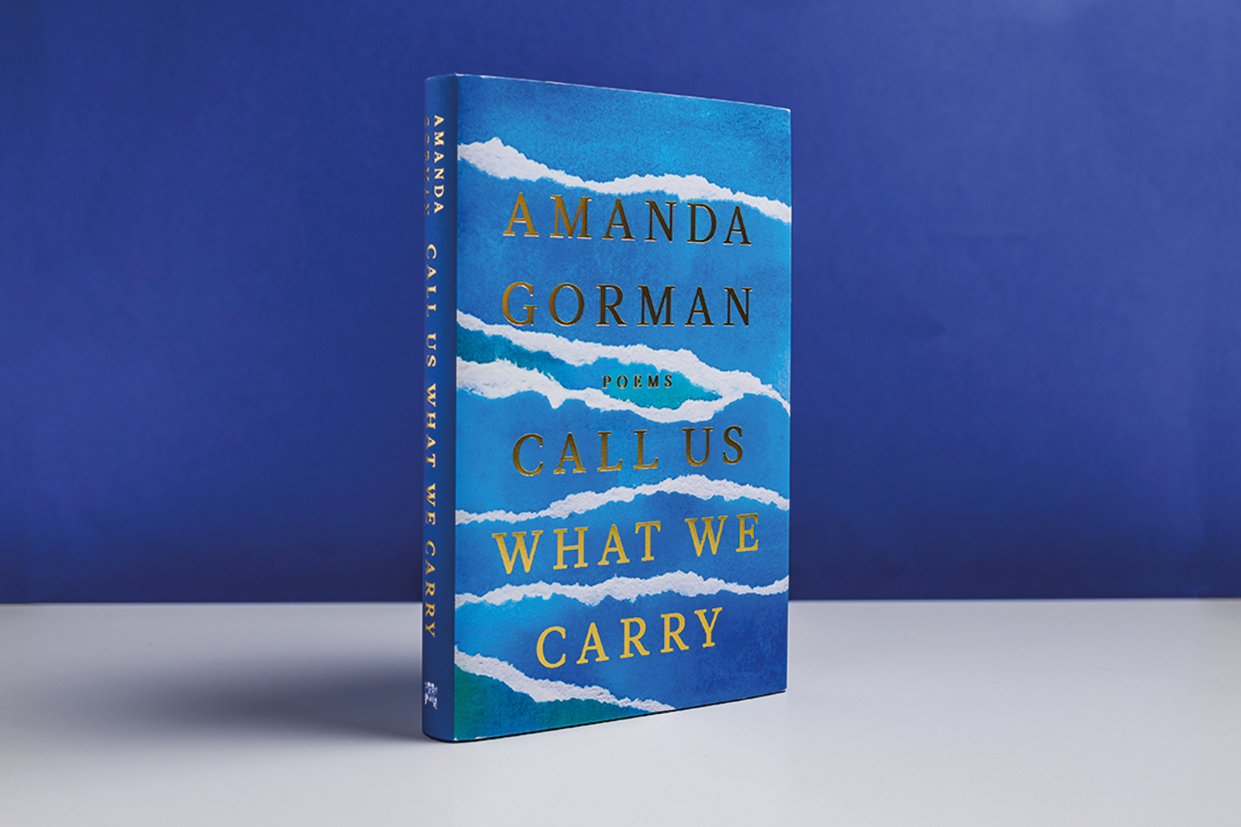A photo of Amanda Gorman's poetry collection, Call Us What We Carry, against a navy blue background with a gold signature overlaid.