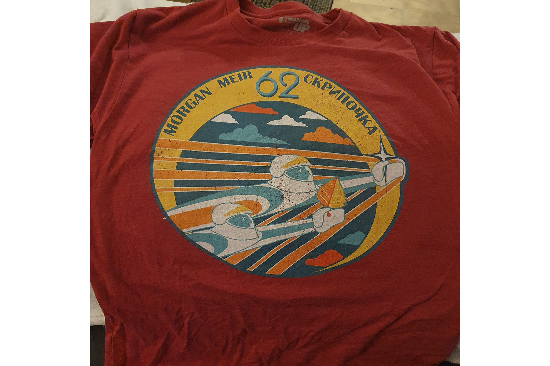 A red T-shirt with a graphic  of astronauts appearing as if they are flying on it