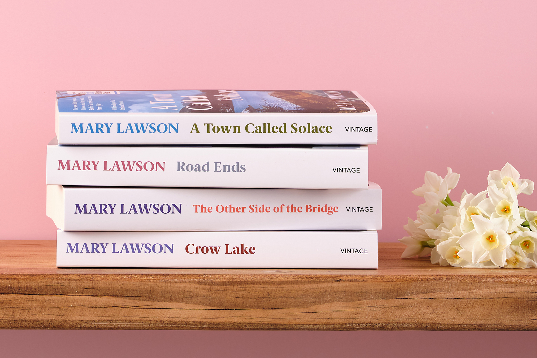 Mary Lawson's books stacked against a pink background with a flower to the right