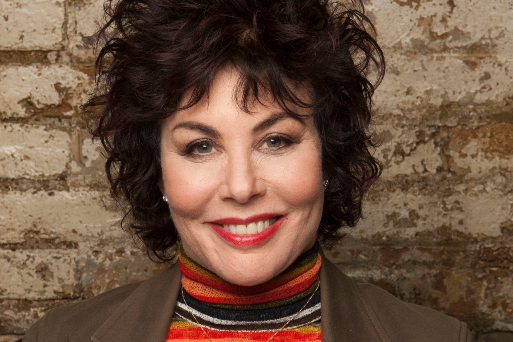 Ruby Wax smiles in front of a brick wall.