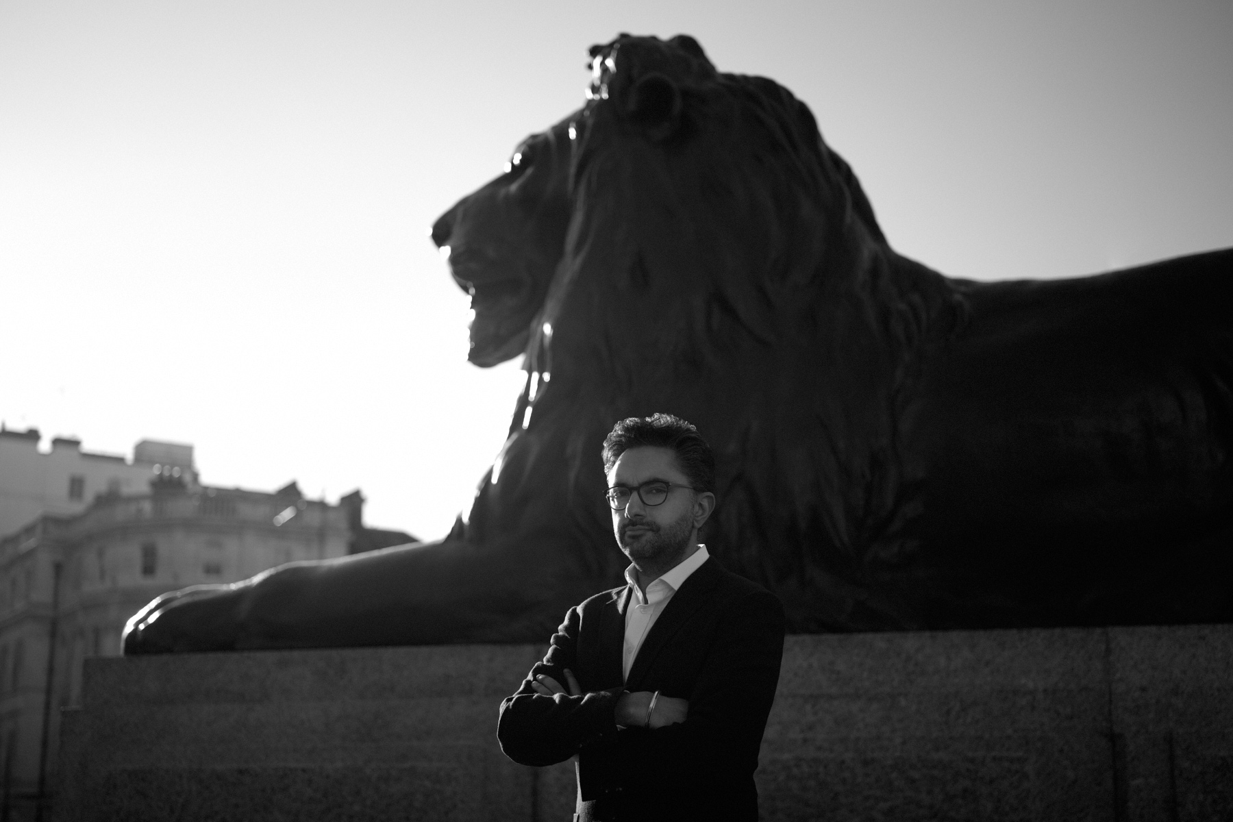 Image of Sathnam Sanghera standing by a lion in Trafalgar square