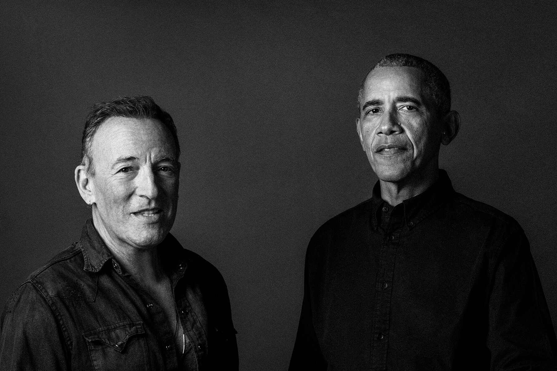 Former President Barack Obama and Bruce Springsteen standing side by side, against a dark background.