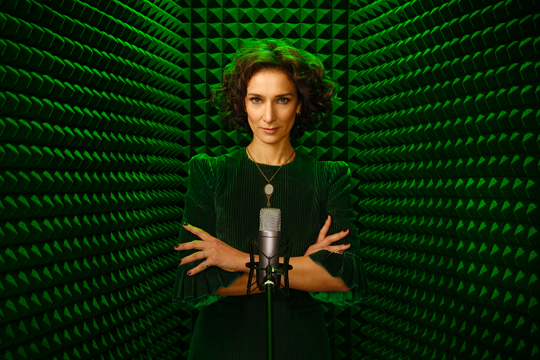 A photo of actor Indira Varma, in a green-lit sound booth.