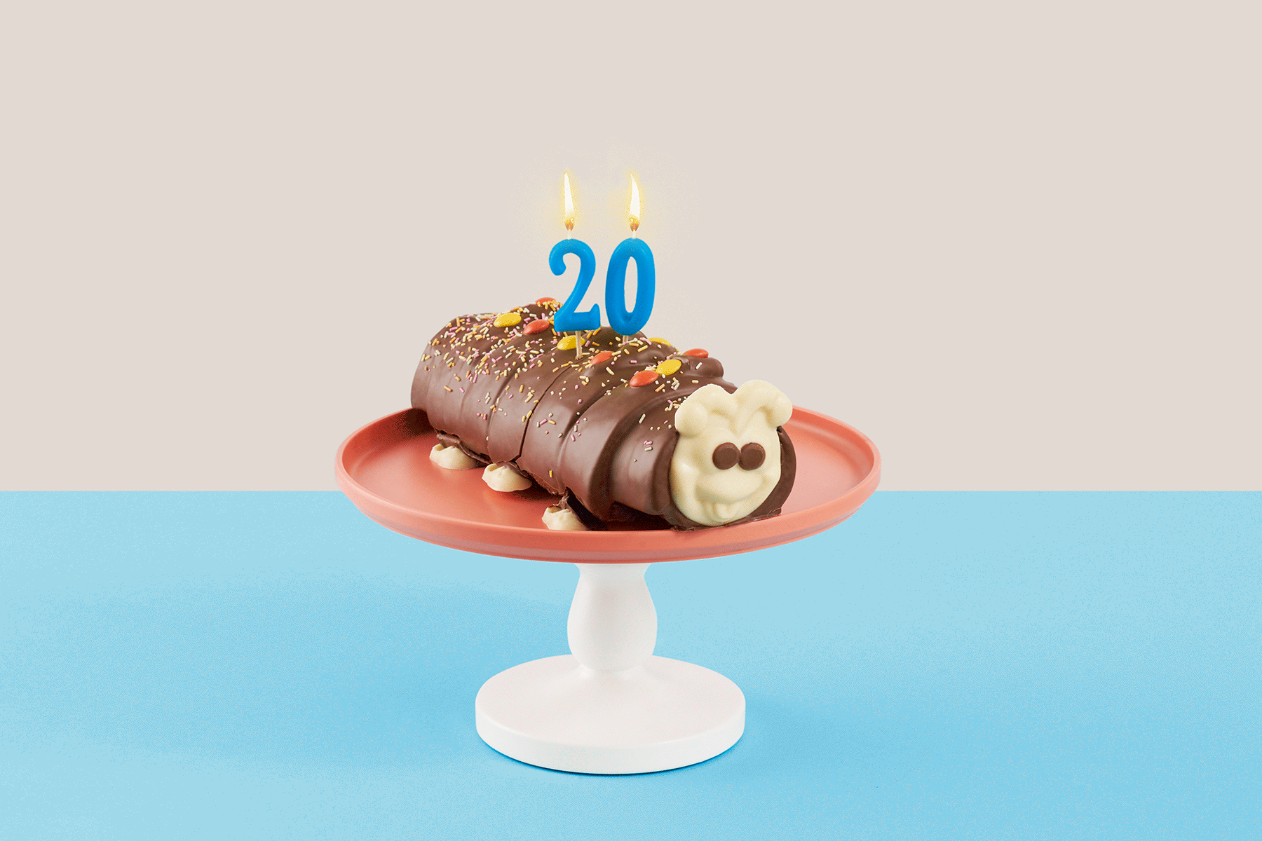 A photo of a caterpillar cake with candles shaped like the number twenty atop; the candles flicker