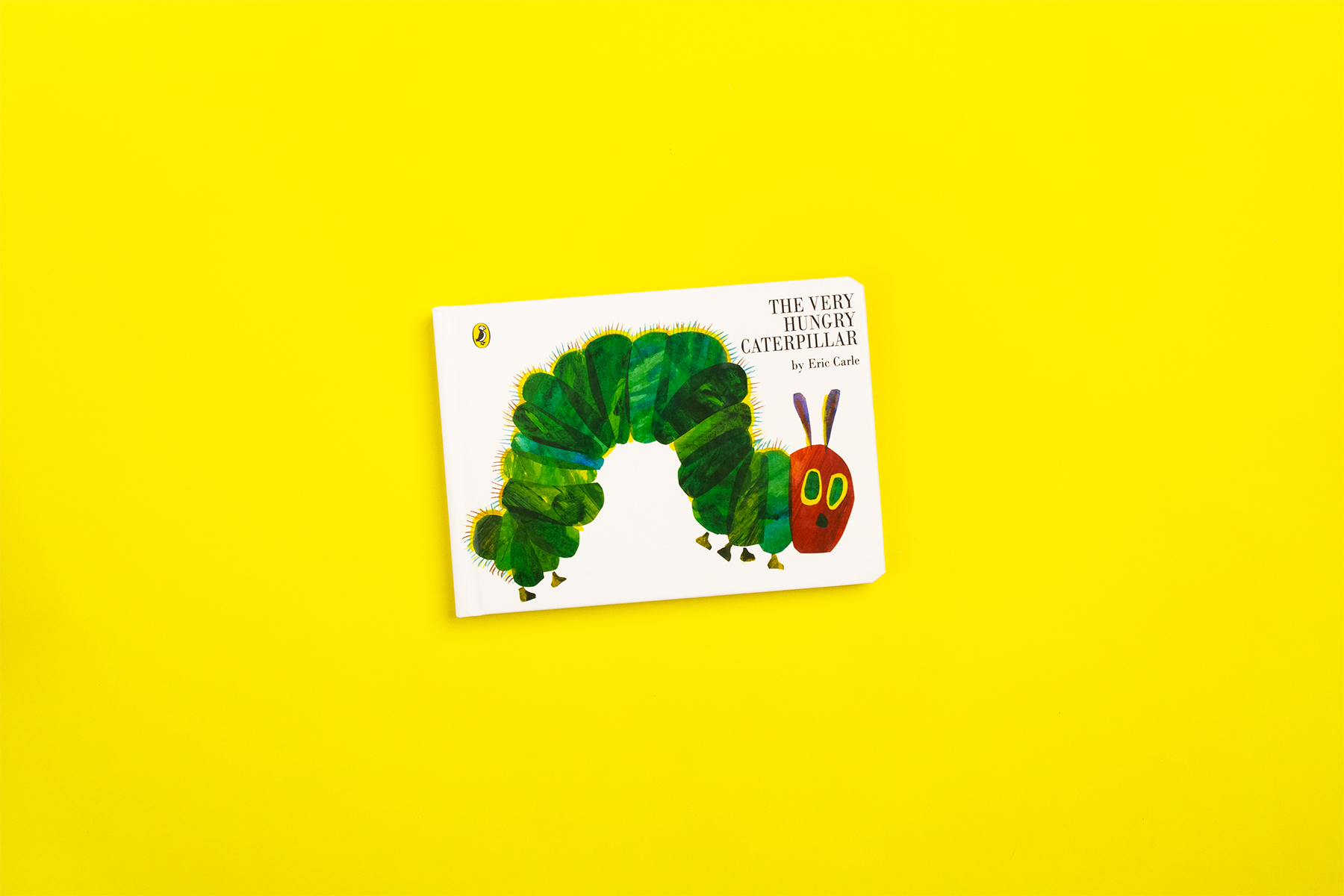A photo of the book The Very Hungry Caterpillar by Eric Carle on a plain yellow background