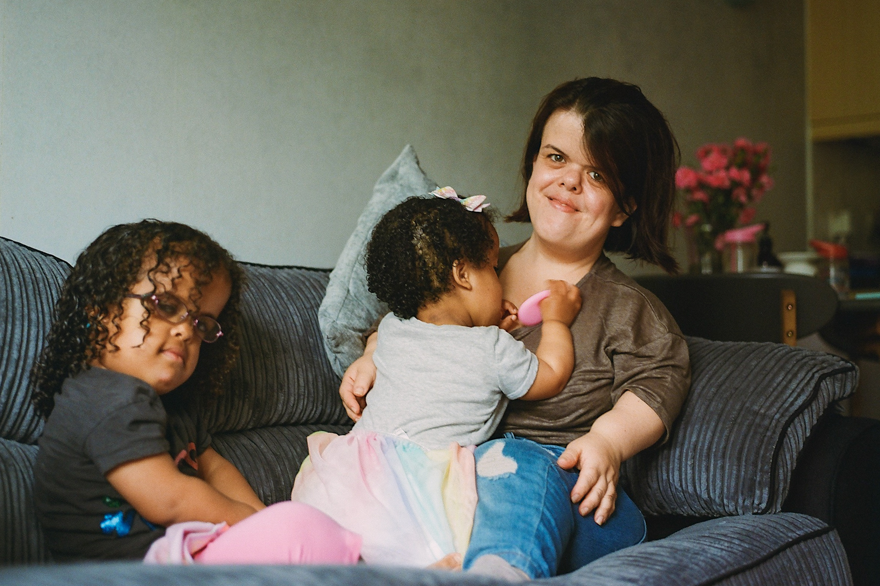 A photo of mum Cathy sitting on her sofa at home with her youngest child in her lap and her eldest sitting next to her looking at the camera