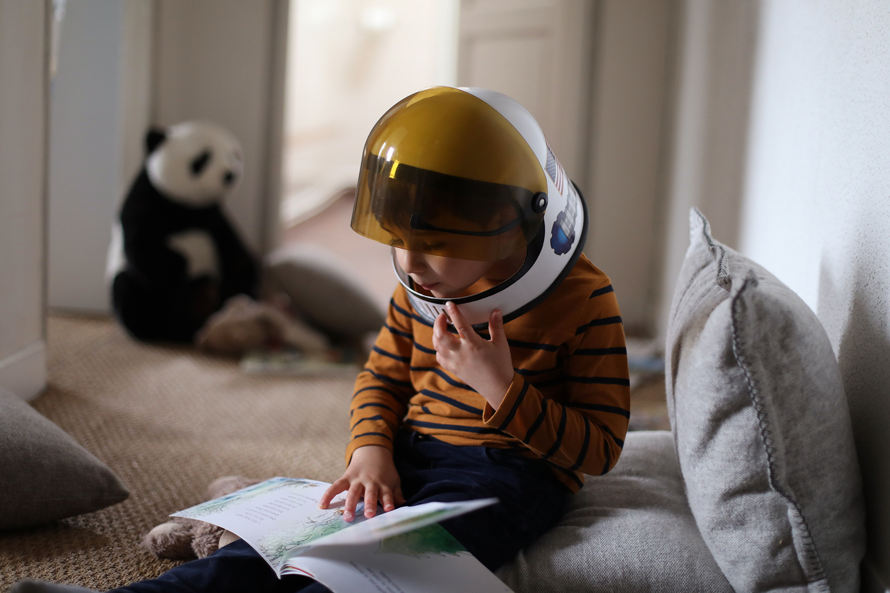 A photo of a little book wearing a space helmet whilst he reads his favourite book