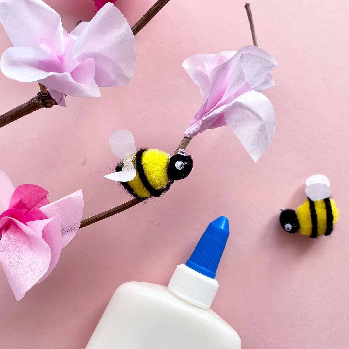Photo of pom pom bee being stuck onto twig alongside tissue paper cherry blossoms with glue