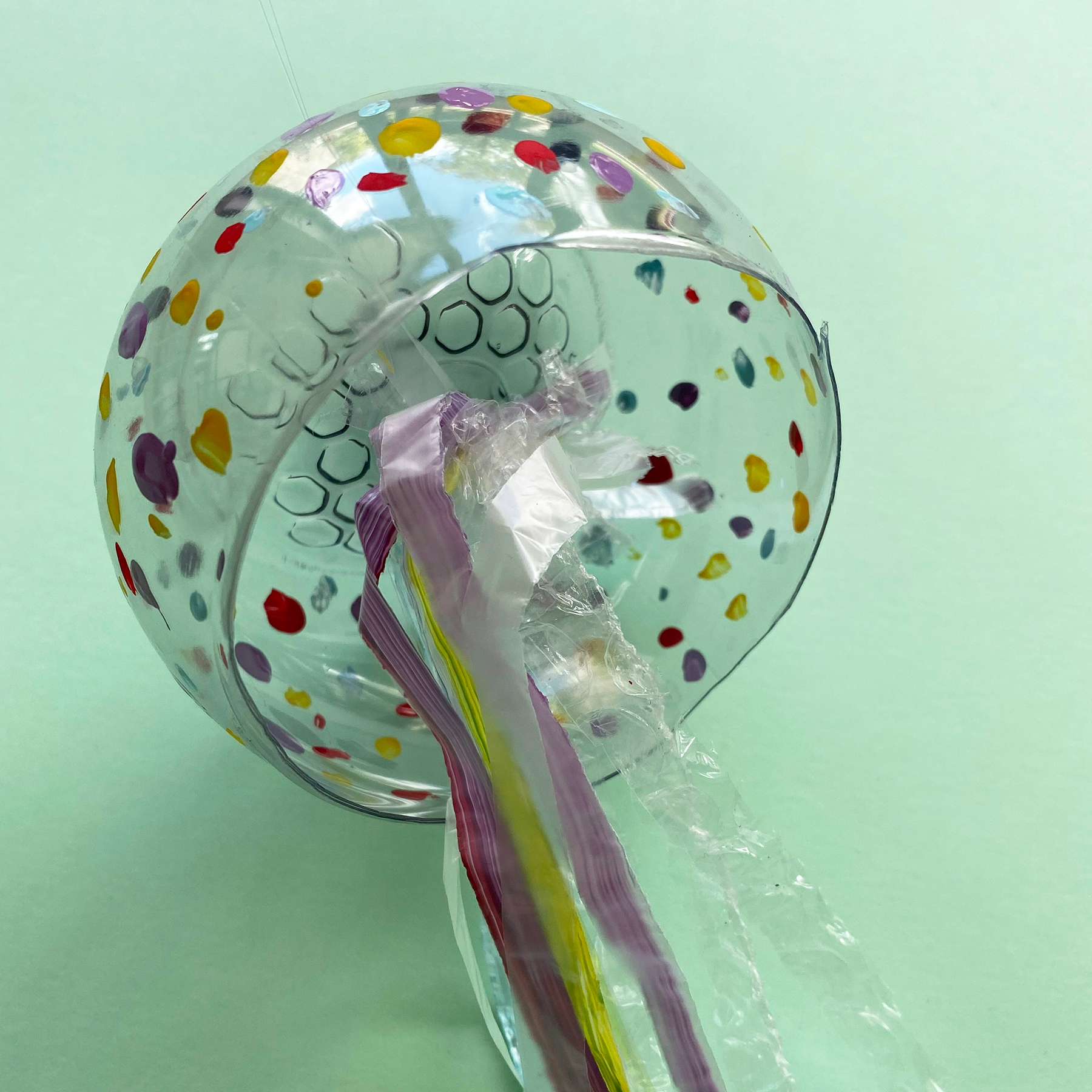 A photo of the plastic bag, cellophane and bubble wrap strips being tied inside the plastic bottle bottom with clear string on a mint green background
