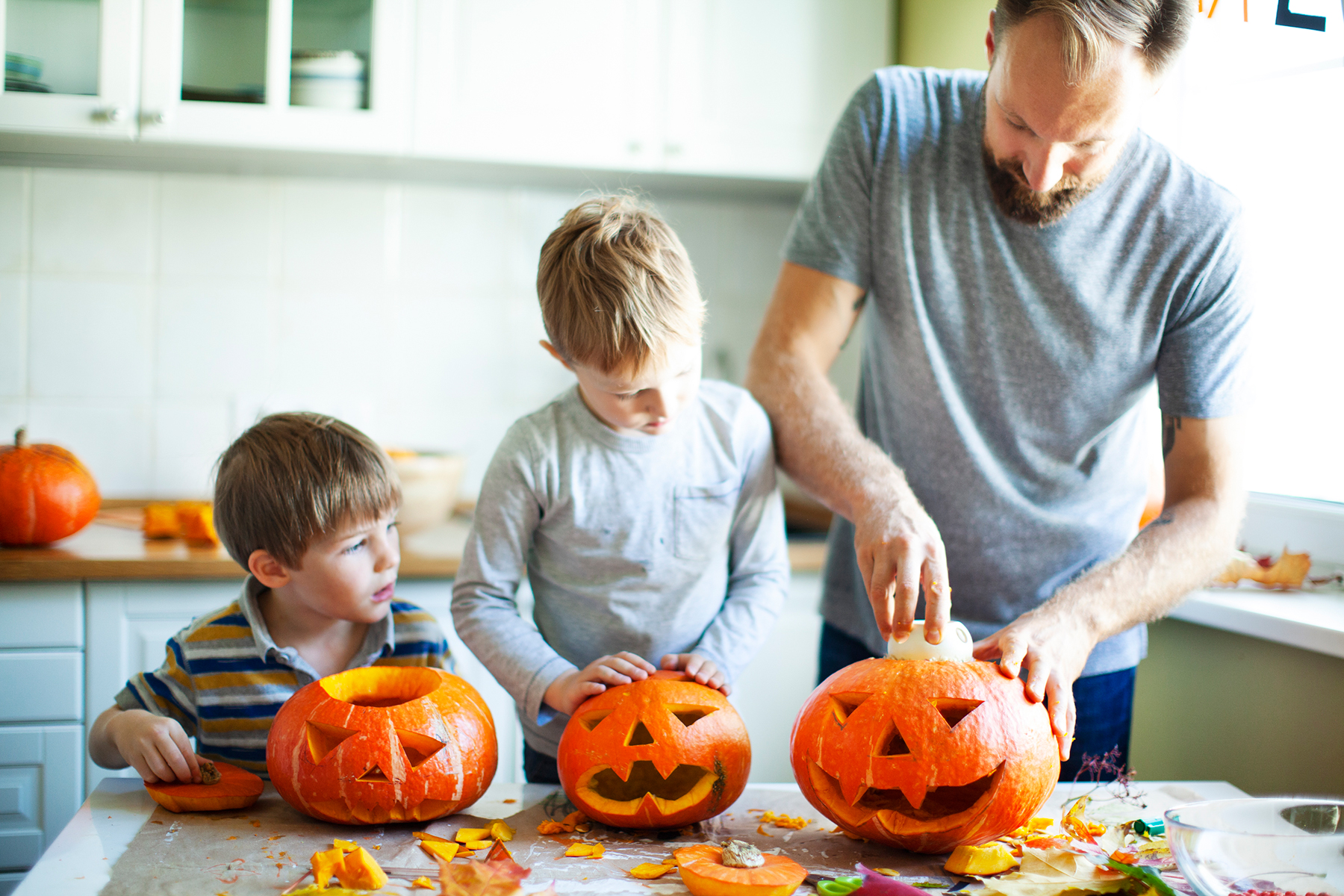 A photo of a dad and his two sons carving pumpkins together in the kitchen