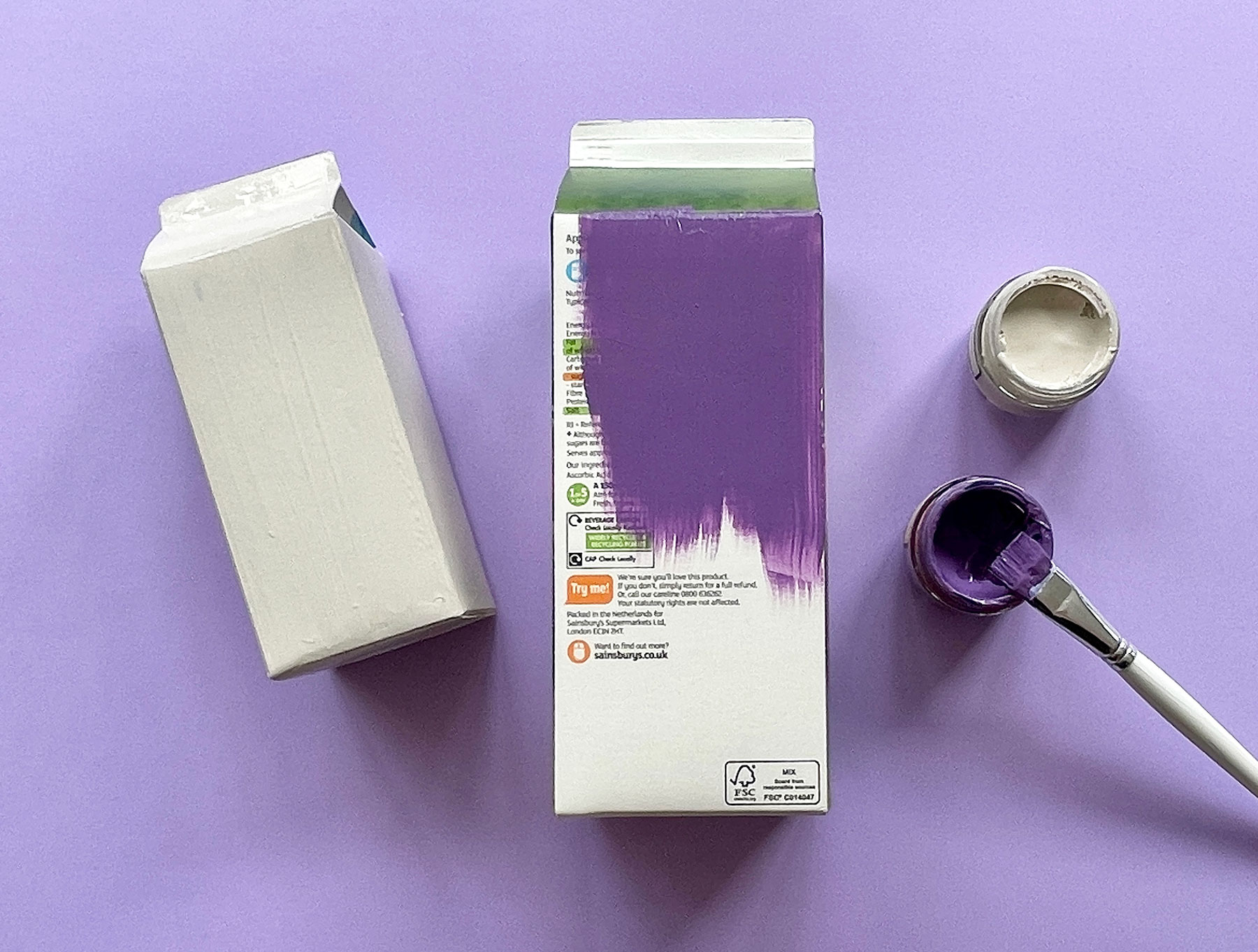 A photo of two juice cartons being painted with purple and grey paint on a light purple background
