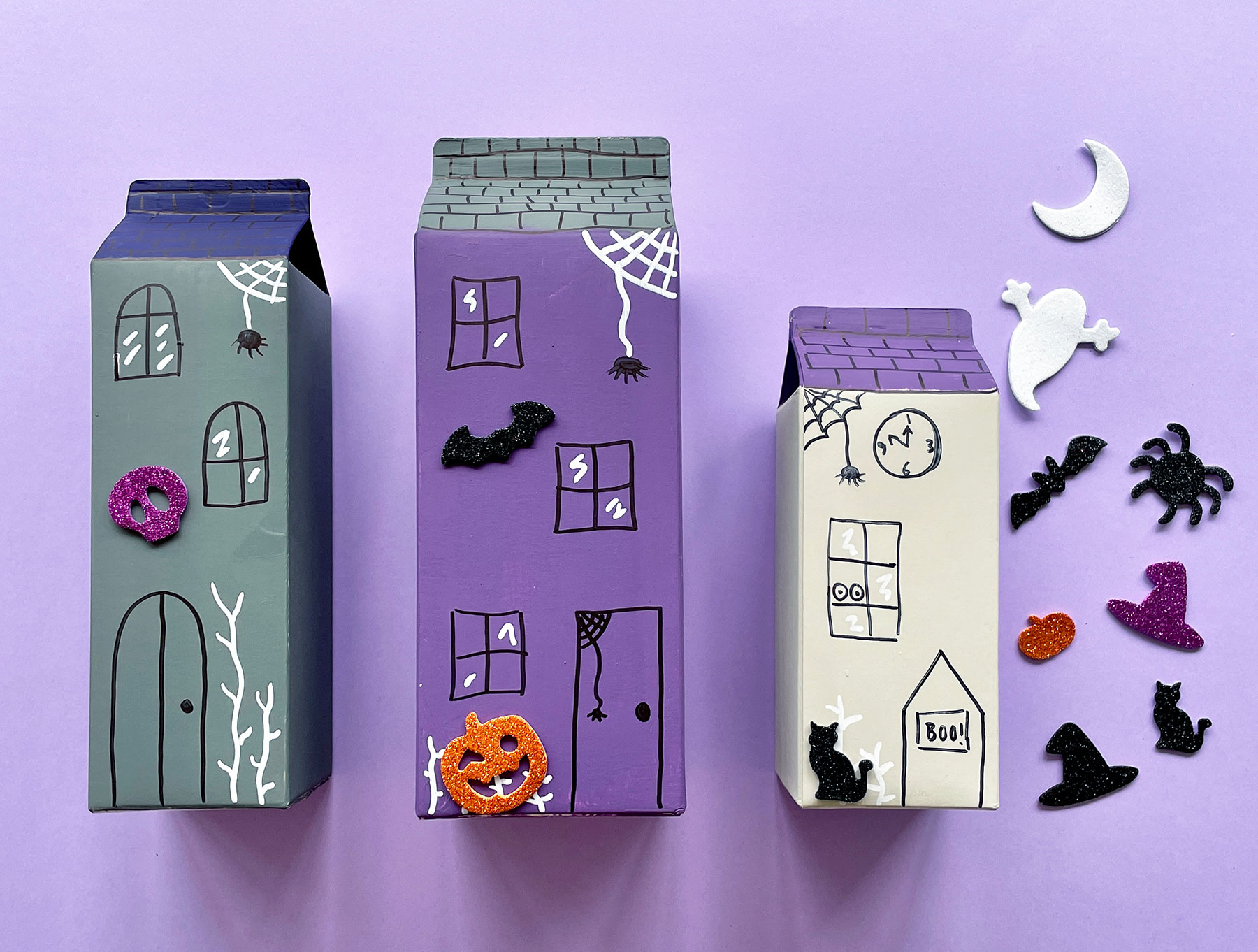 A photo of three cartons, painted to look like houses having foam stickers stuck onto them
