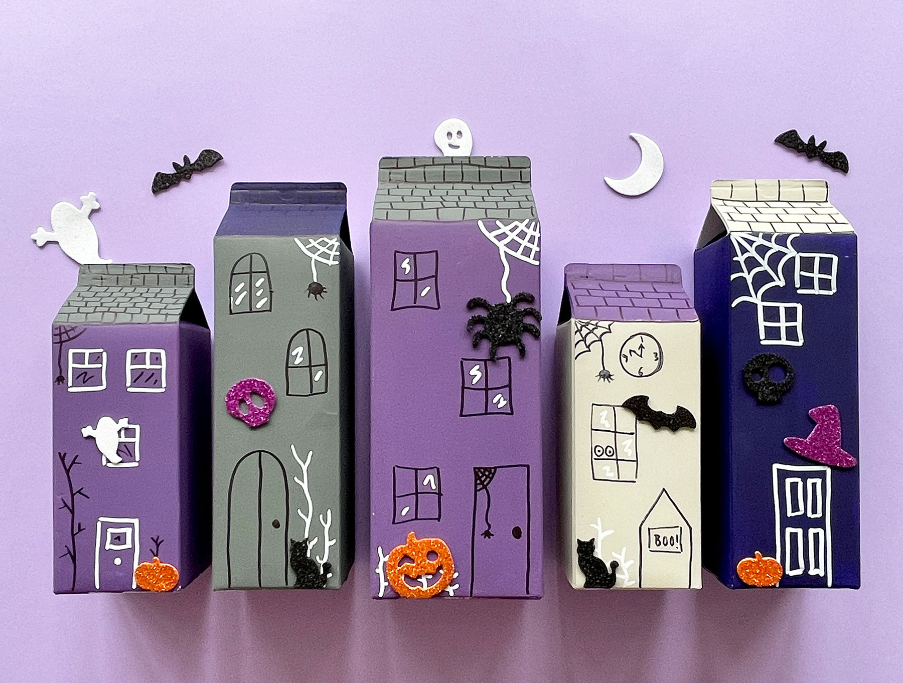 A photo of a DIY haunted village made out of empty juice cartons on a light purple background