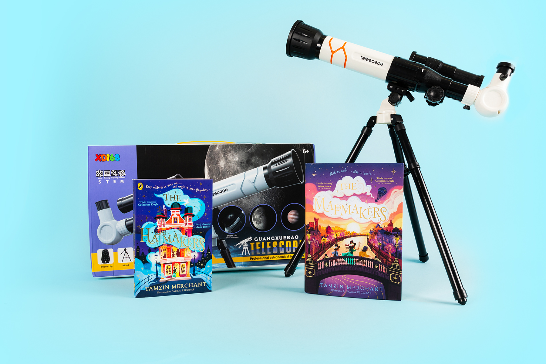 A photo of the books The Hatmakers and The Mapmakers alongside a telescope, against a light blue background