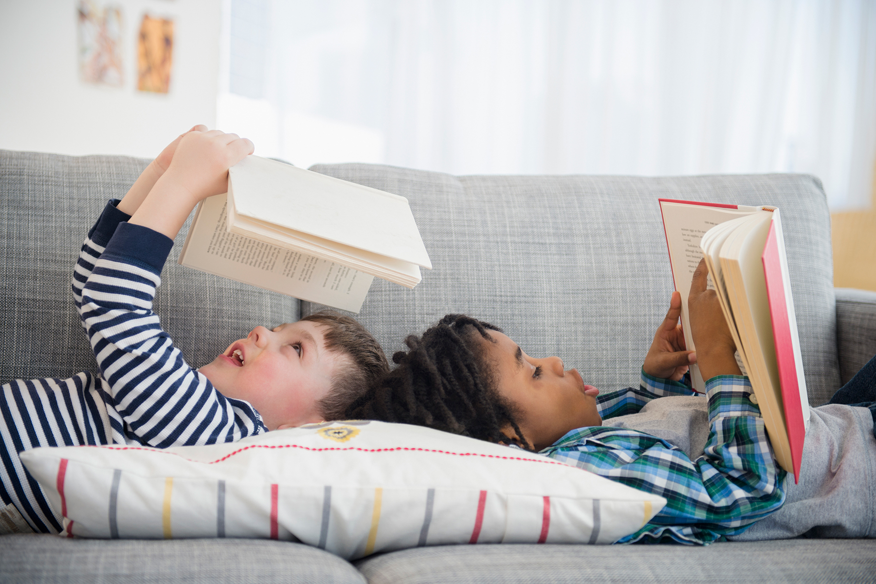 A photo to two young boys laying down on a sofa and reading books together