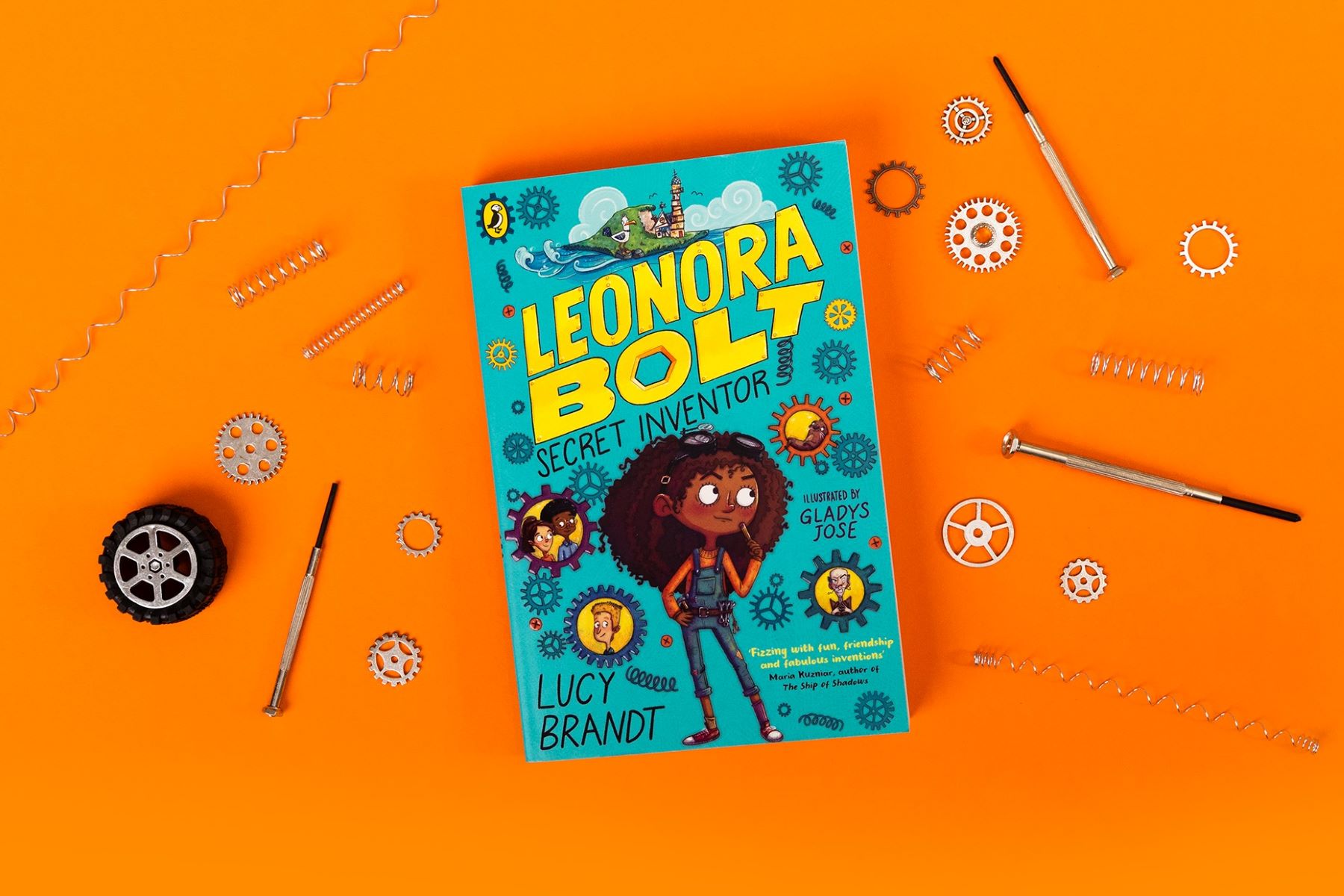 A photo of a copy of Leonora Bolt: Secret Inventor on a bright orange background with tools and cogs surrounding the book